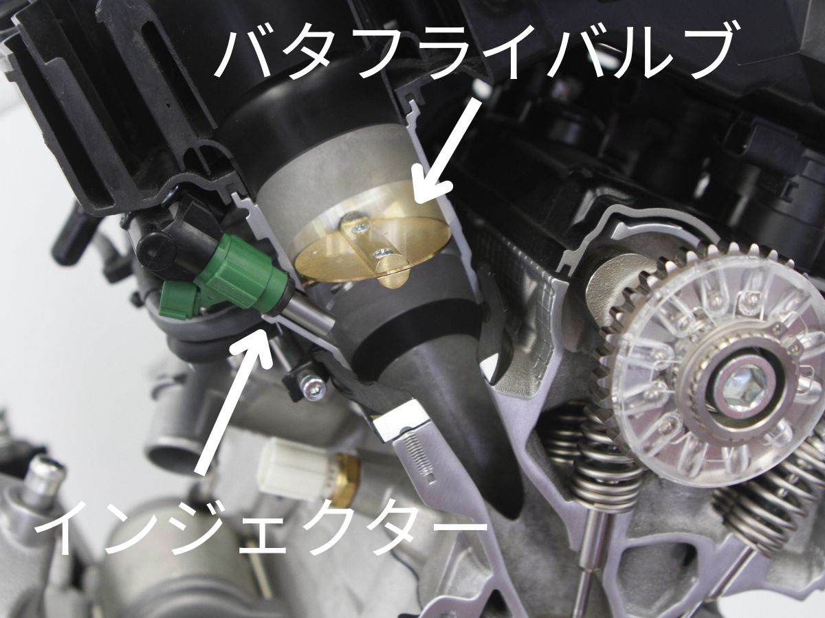 GSX-R1000Rの吸気系のカットモデルで中央の金色の円盤のようなパーツがバタフライバルブでエンジンが吸い込む混合気の量を調整している。写真はスロットル全閉の状態で、スロットルが開くと円盤が時計回りに回転し、通路の中で90度になった状態が全開。エンジンはバタフライバルブが開いて混合気の流れが良くなると、その分だけ回転数が上がる。