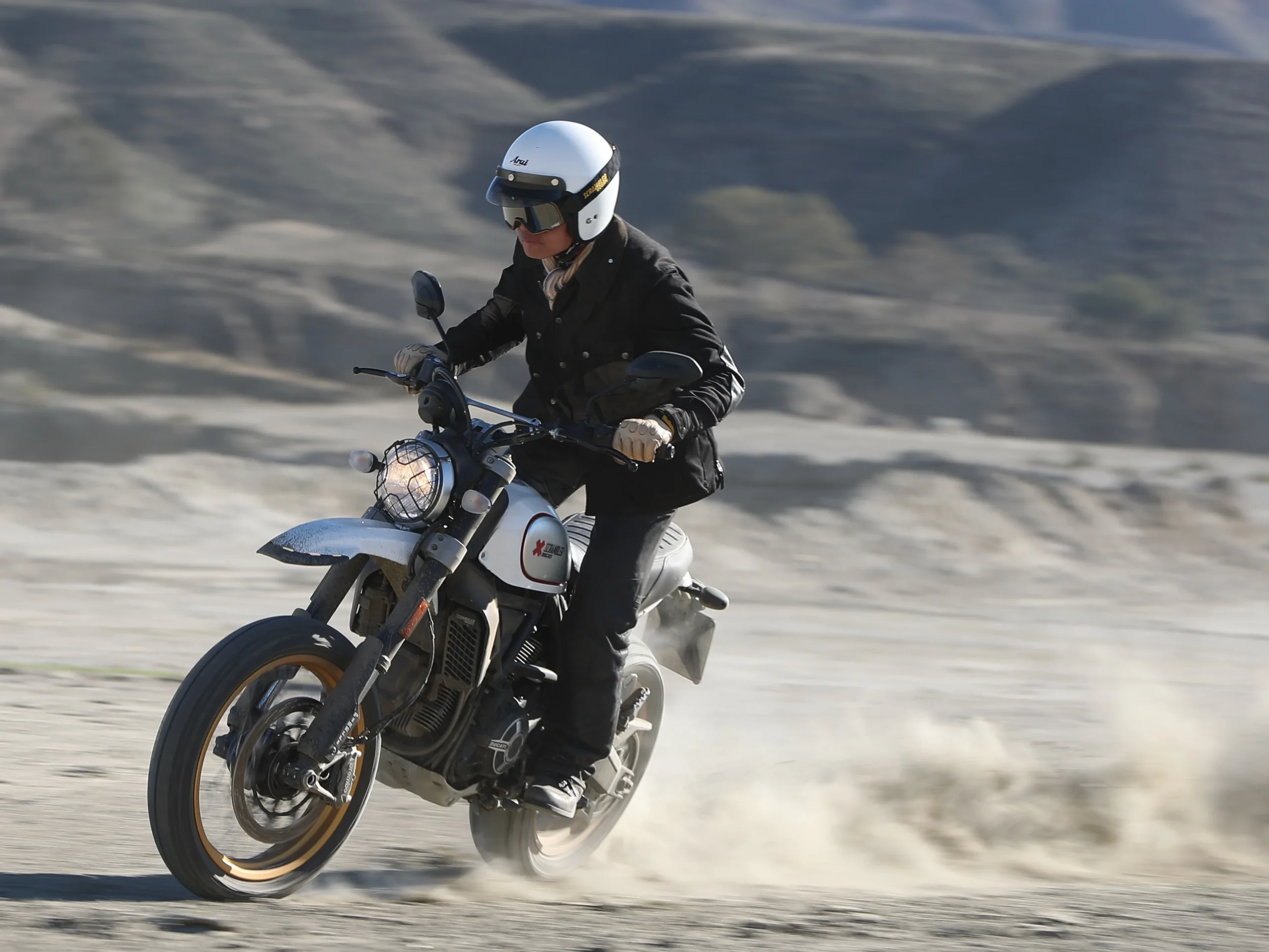 ドゥカティの『スクランブラー』モデル、Scrambler Desert Sledでダート走行を行う筆者・谷田貝　洋暁。『スクランブラー』は、こんなカジュアルなウエアも似合うのがいいところ。クラシックタイプのジェットヘルメットにゴーグル、バイザーに革やコットン生地の長丈のライディングジャケットを組み合わせるとレトロ感がアップするぞ！